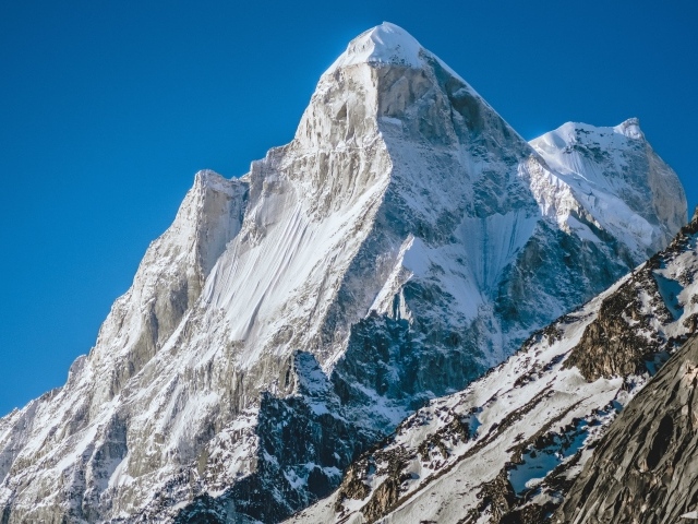 Острая вершина заснеженной горы под голубым небом