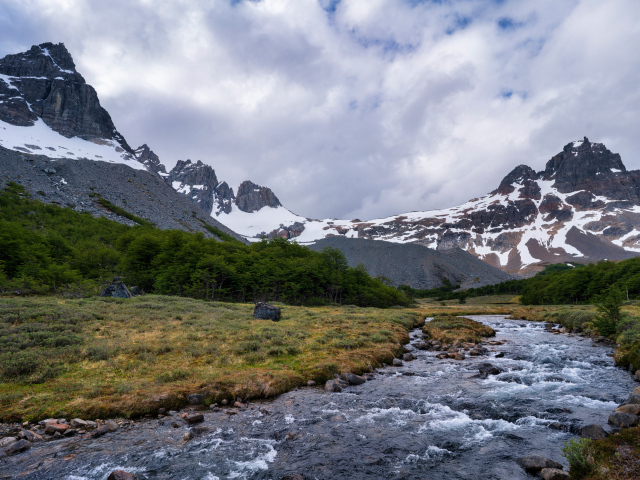 Быстрая река у заснеженных гор под густыми белыми облаками