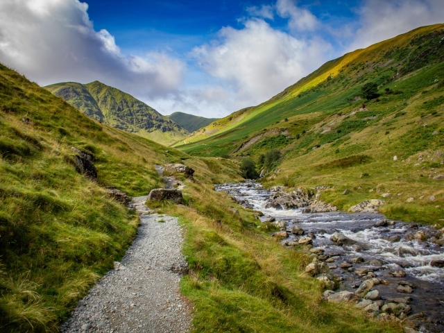 Тропа у реки на фоне покрытых зеленью гор 
