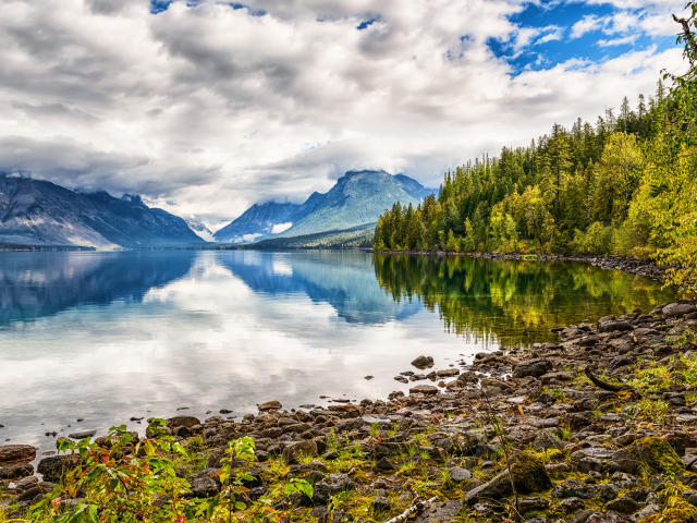 Камни на берегу горного озера с белыми облаками 
