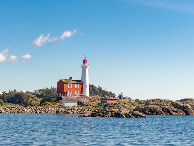 Маяк на каменном берегу моря под голубым небом 