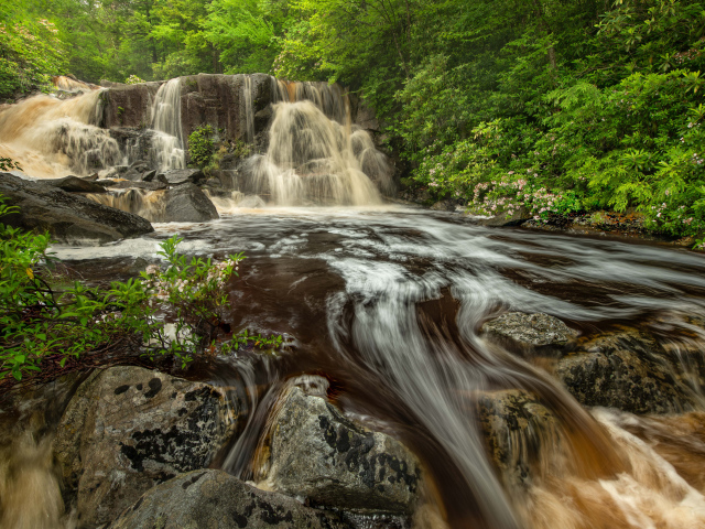 Быстрая холодная вода водопада стекает по большим камням