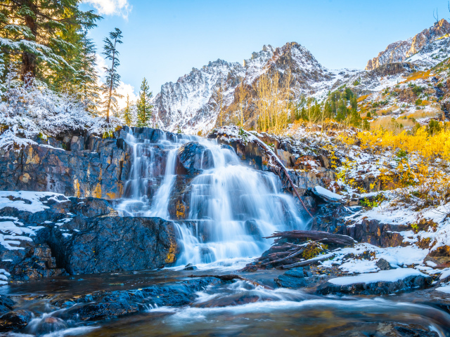 Водопад стекает по покрытым снегом камнях в горах