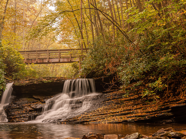 Водопад стекает по камням под мостом осенью