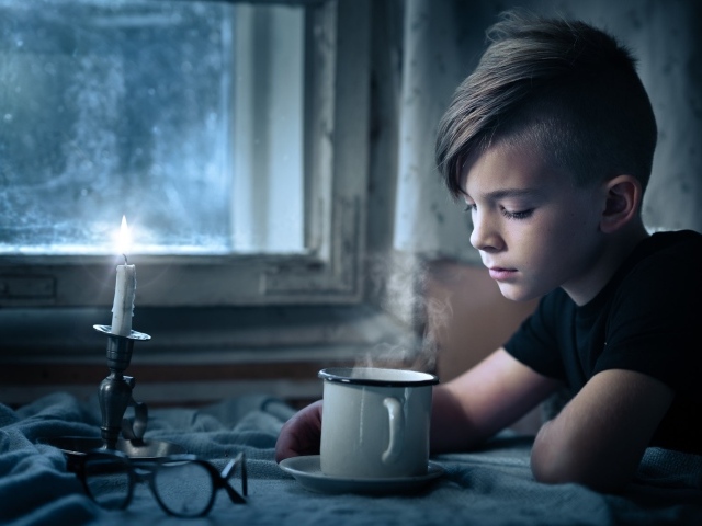 Маленький мальчик сидит за столом при свете свечи 