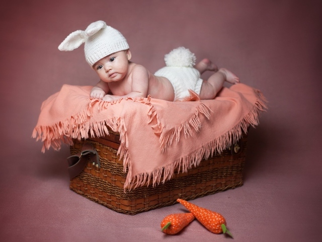 Маленький ребенок в костюме зайчика лежит на корзине 