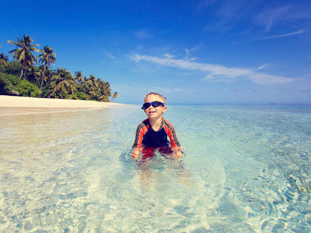 Мальчик в очках сидит в воде на пляже 