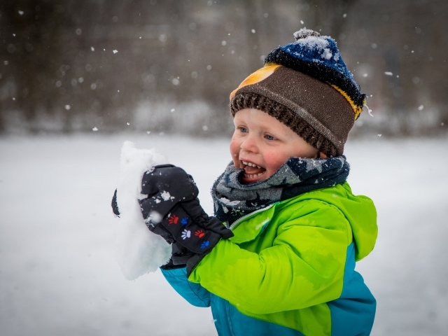 Веселый маленький мальчик со снегом в руках 