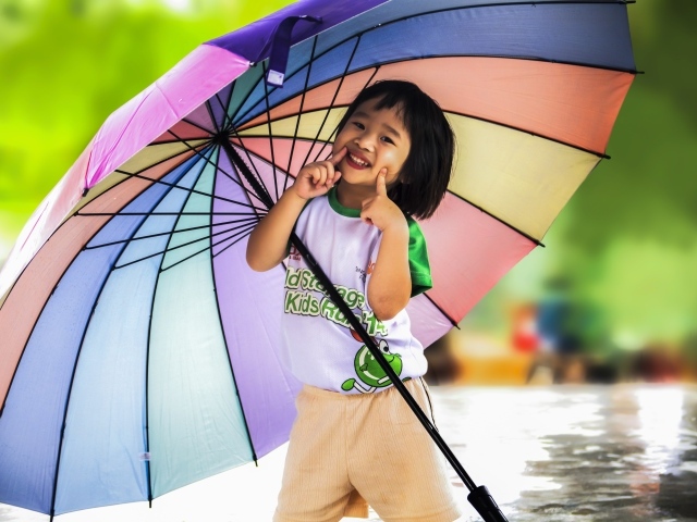 Маленькая девочка азиатка под большим разноцветным зонтом 