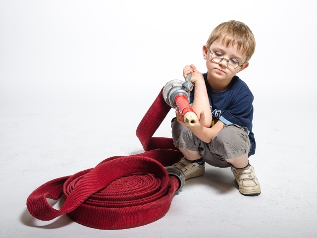 Маленький мальчик на белом фоне играет в пожарного