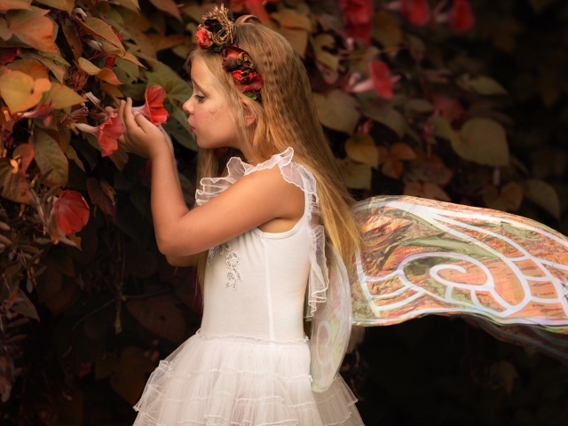 Маленькая девочка в костюме феи стоит у цветов