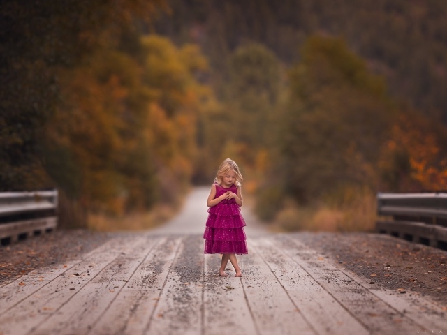 Маленькая девочка в платье стоит на мосту 