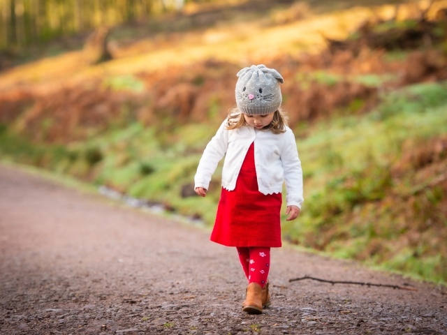Маленькая девочка в красном платье идет по дороге 