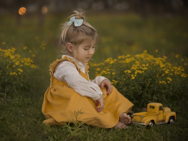 Маленькая девочка в желтом платье сидит на траве 