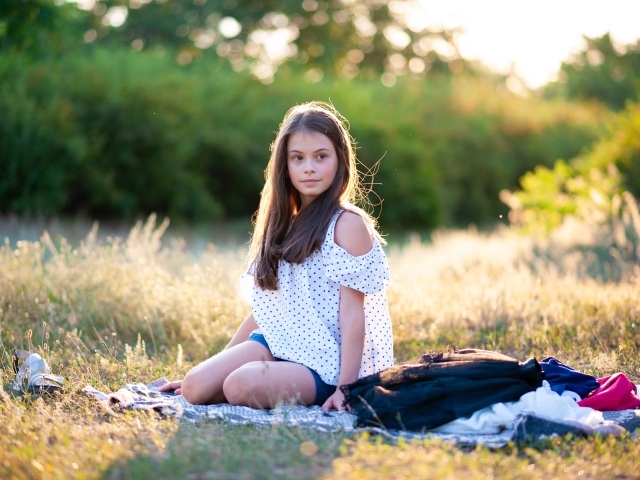 Маленькая девочка сидит на покрывале на земле 