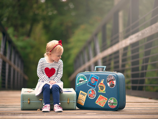 Маленькая девочка сидит на мосту с чемоданами