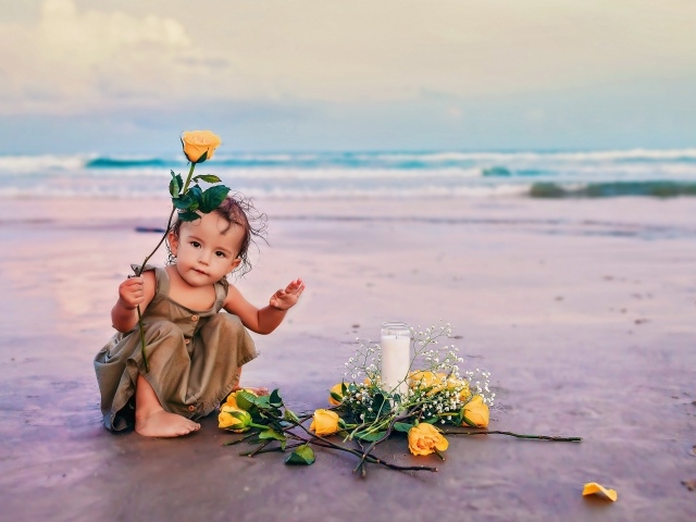Маленькая девочка сидит на песке с розами 