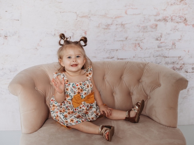 Маленькая девочка сидит на диване у стены