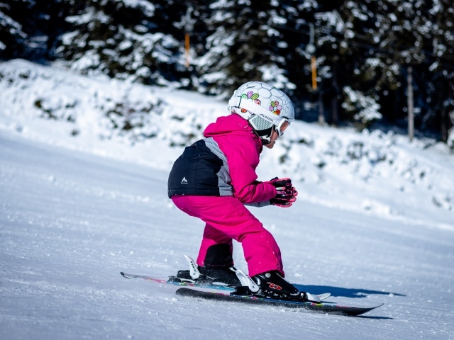 Маленькая девочка едет на лыжах по снегу