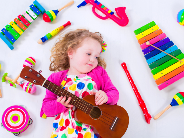Маленькая девочка с гитарой и игрушечными музыкальными  инструментами 