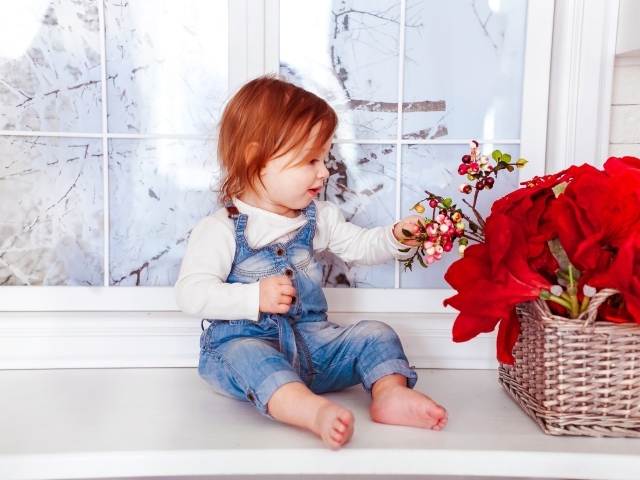 Маленькая рыжеволосая девочка сидит у корзины цветов 