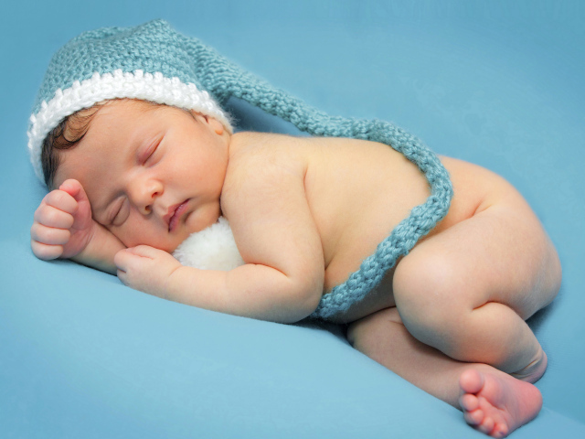 Маленький спящий ребенок в шапке на голубом фоне 