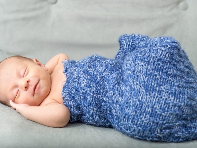 Маленький грудной ребенок в синем вязаном покрывале 