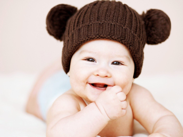 Улыбающийся грудной ребенок в коричневой шапке