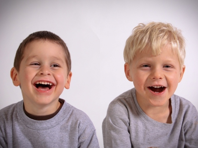 Два маленьких мальчика смеются на сером фоне