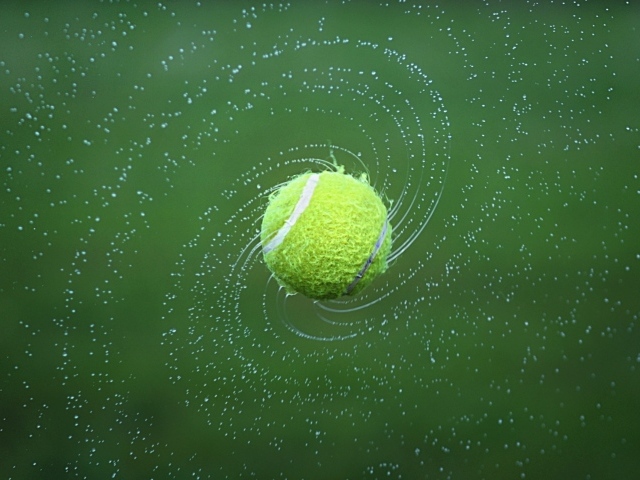 Теннисный мяч в брызгах воды на зеленом фоне
