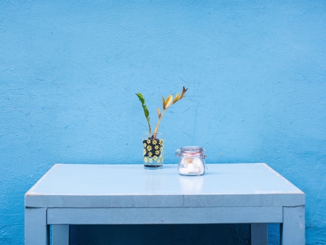 Стол с цветком стоит у голубой стены 