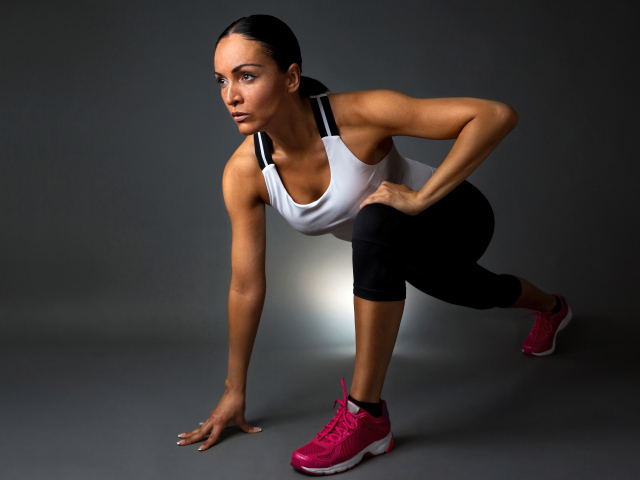 Девушка спортсменка в стойке на сером фоне 