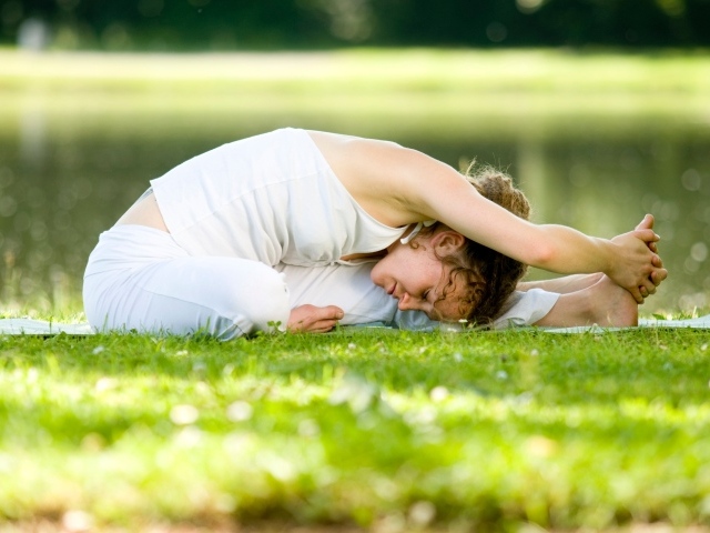 Девушка в белом костюме занимается йогой на траве