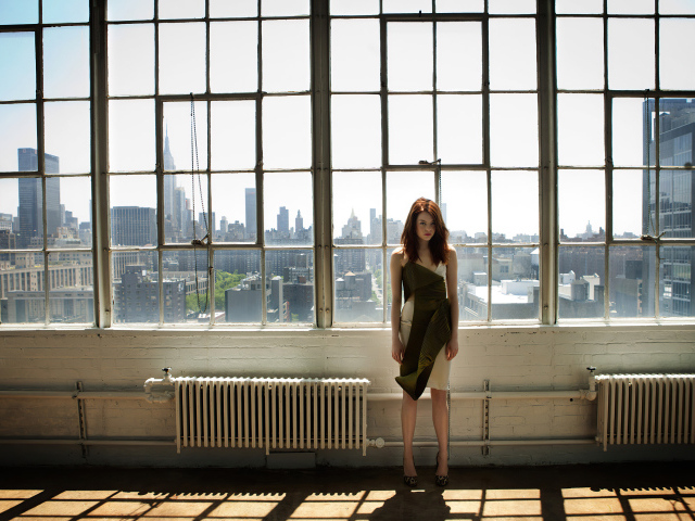 Популярная актриса Эмма Стоун стоит у большого окна
