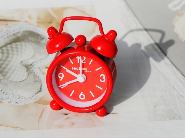 Маленький красный будильник стоит на столе 