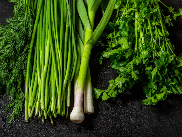 Зеленый лук с петрушкой и укропом на черном столе 