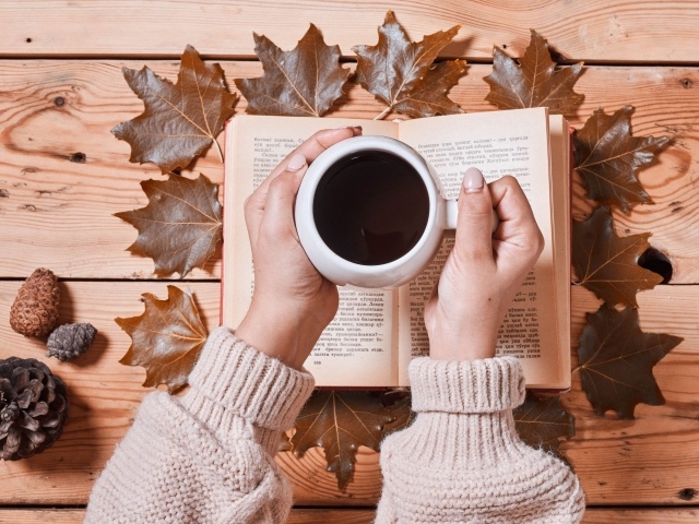 Чашка кофе в руках на столе с книгой и листьями