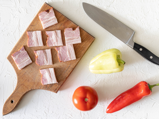 Кусочки ветчины с перцем и помидором на столе 
