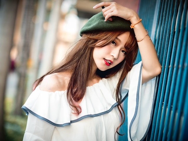 Девушка азиатка в берете стоит у стены 