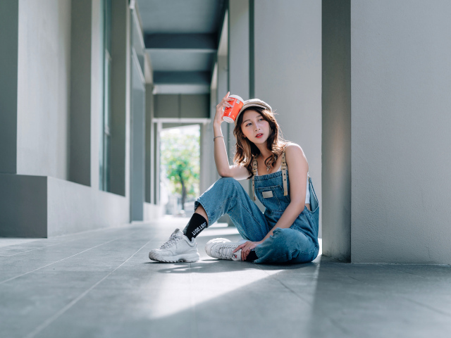 Девушка азиатка в синем комбинезоне с кофе в руке 