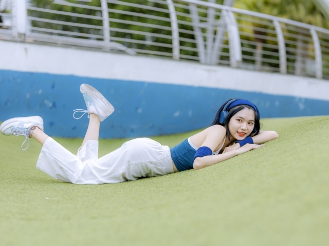 Девушка азиатка в наушниках лежит на полу 