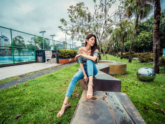 Девушка азиатка в джинсах сидит в парке 