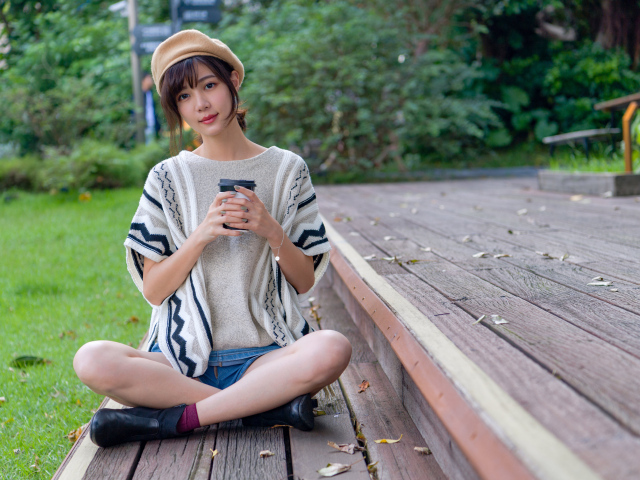 Девушка азиатка сидит с кофе в осеннем парке 