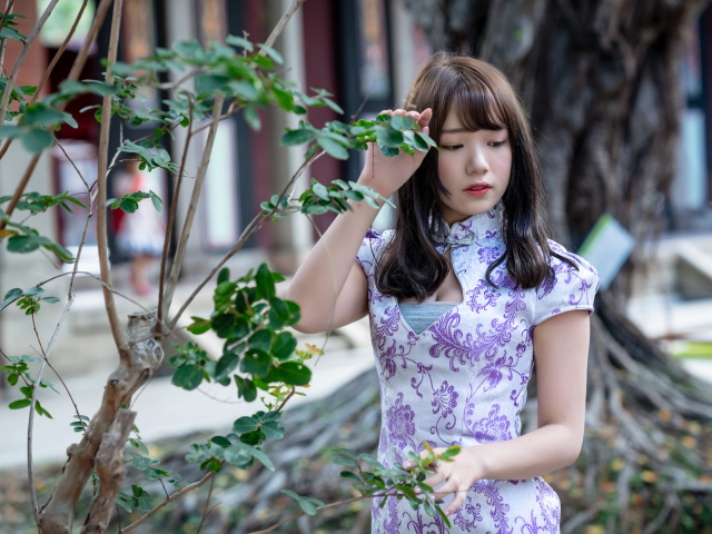 Красивая девушка азиатка в платье стоит у дерева 