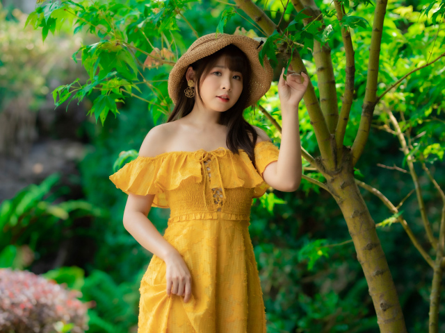 Красивая девушка азиатка в желтом платье   шляпе у дерева