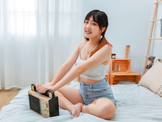 Красивая девушка азиатка с магнитофоном на кровати 