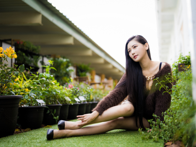 Красивая азиатка сидит на земле у цветов