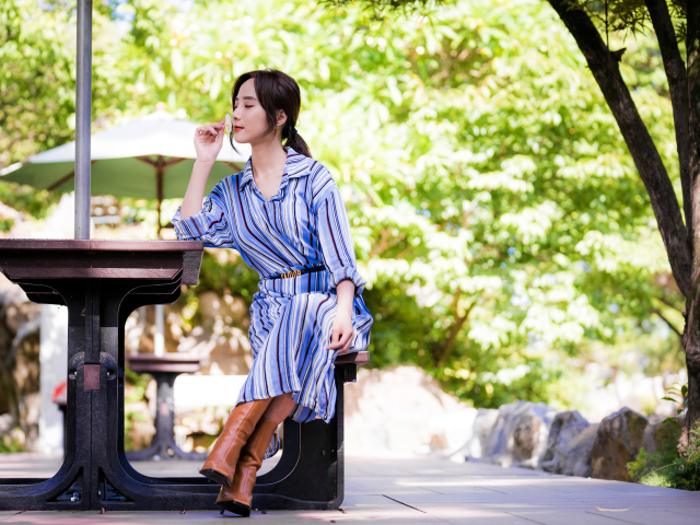 Красивая девушка в платье сидит за столиком в парке