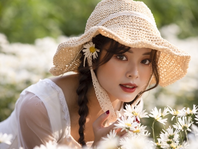 Красивая девушка в шляпе на поле с ромашками 