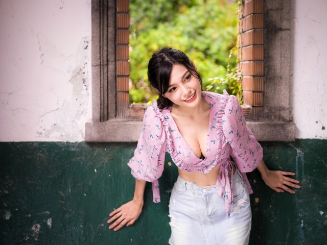 Улыбающаяся девушка азиатка стоит у окна 